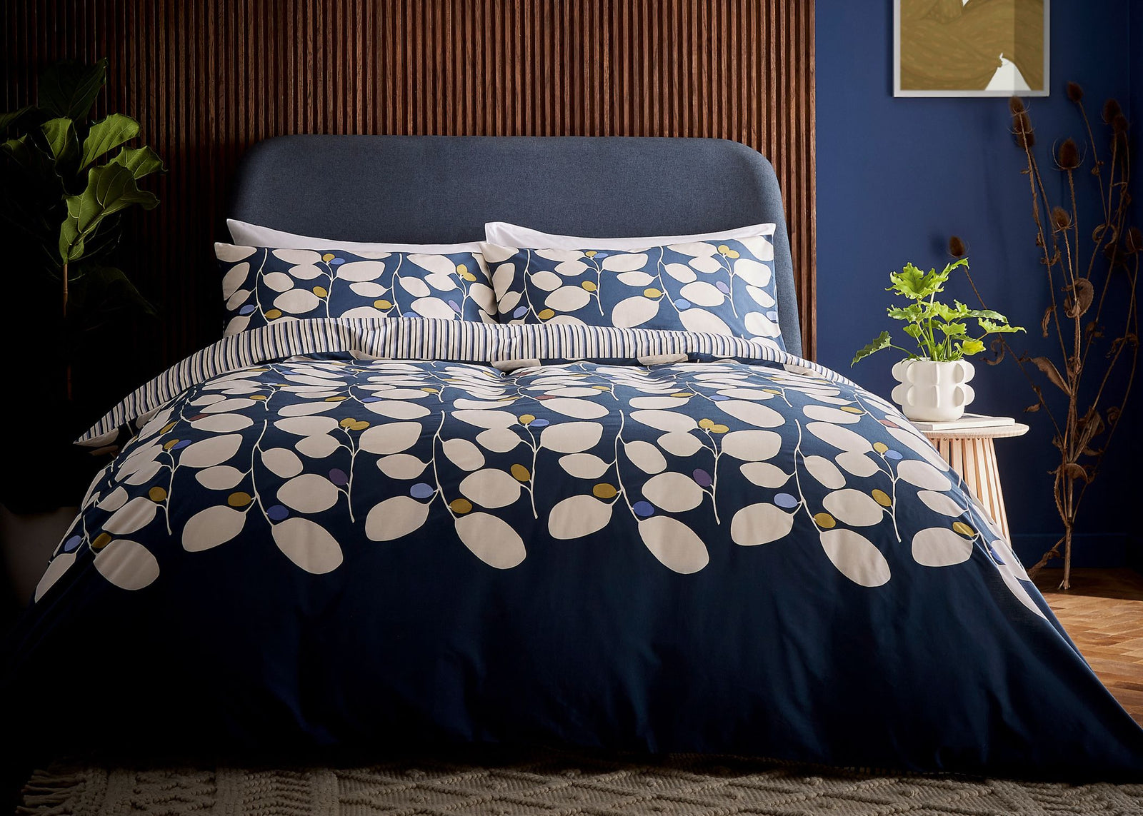 Navy blue floral bedding set on a bed in a bedroom with a plant and side table.